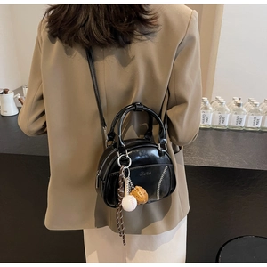 Detail der schwarzen glänzenden Handtasche mit Baseball-Anhängern und Kontrastnaht