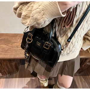 Detail of a black patent leather Boston bag with gold logo and woven pendant