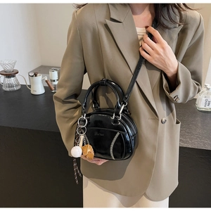 Detail der schwarzen Lackledertasche mit weißen Baseballnähten und Handschuhanhänger