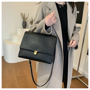 Close-up of black pebble leather handbag with gold buckle on a grey wool coat