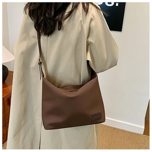 Vue détaillée du sac bandoulière marron foncé avec logo et finition mate sur un trench