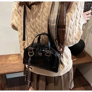 Detail of a black leather Boston bag with gold hardware and woven charm accessory