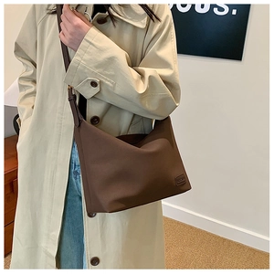 Détail du sac bandoulière en similicuir marron foncé avec logo gaufré sur trench-coat beige
