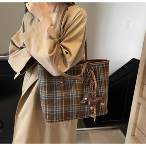 Detail of green plaid tote bag with dachshund charm and brown leather straps on a beige coat