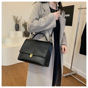 Detail of black textured leather bag with gold buckle on a model in a grey coat