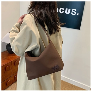 Détail d'un sac hobo marron foncé avec logo de marque porté au dos par un mannequin