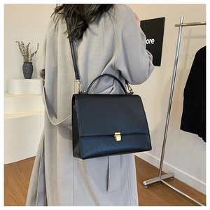 Detailed view of black litchi grain leather crossbody bag with gold metal buckle