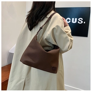 Détail d'un sac demi-lune marron foncé avec bandoulière nouée et logo embossé de cuir