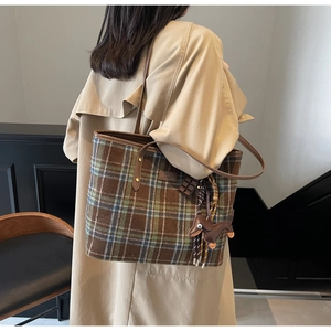Close-up of a large plaid tote bag in wool with brown leather straps and dog charm