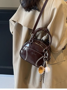 Retro dunkelbraune Bowlingtasche mit weißen Nähten und Baseball-Anhängern am Trenchcoat
