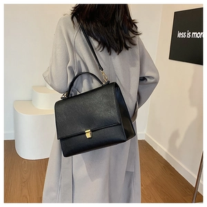 Detail of black pebbled leather crossbody bag with gold hardware on a model