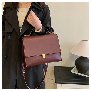 Detail of burgundy textured leather handbag with gold buckle on a black trench coat