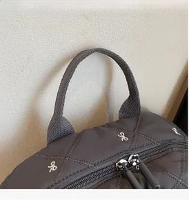 Detail of dark gray quilted backpack fabric with white bow embroidery and top handle