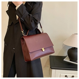 Close-up of wine red lychee pattern leather handbag with gold metal lock and shoulder strap