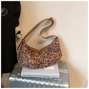Détail du sac demi-lune imprimé léopard posé sur une valise argentée style urbain