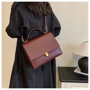 Detail of a vintage burgundy leather crossbody bag on a black coat in a chic setting