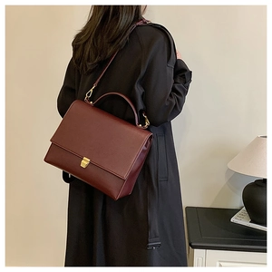 Deep red lychee grain leather crossbody bag with gold buckle shown on black coat