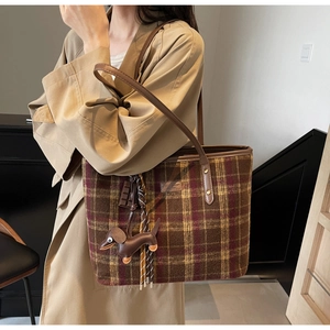Detail of plaid tote bag with leather straps and decorative pendants on a trench coat