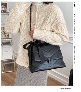 Détail du sac bandoulière en cuir matelassé noir avec un grand nœud en satin et chaîne