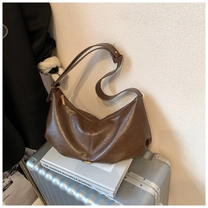Détail du sac hobo en cuir froissé marron foncé avec fermeture éclair dorée sur valise