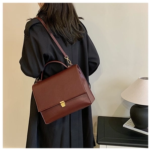 Detail of burgundy lychee leather shoulder bag with golden buckle and top handle