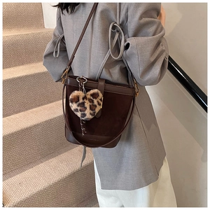 Detail of dark brown bucket bag with leopard heart charm on a textured leather finish