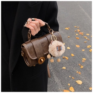 Nahaufnahme einer braunen Vintage-Handtasche mit Metallschloss und Anhänger im Herbststil