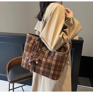 Detail of plaid tote bag featuring thick wool fabric and brown leather handle with dog charm