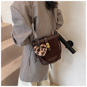 Detail of dark brown bucket bag featuring a leopard heart charm and gold metal clasp