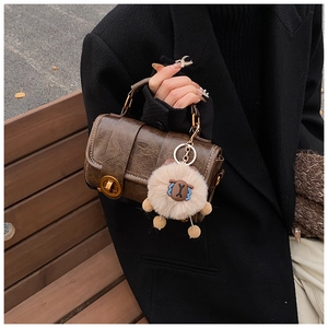 Detail einer braunen PU-Handtasche mit goldenem Drehverschluss und weißer Kontrastnaht