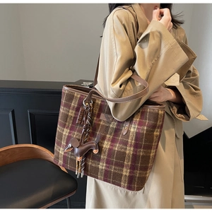 Brown plaid tote bag with dachshund charm carried by a model in a beige trench coat