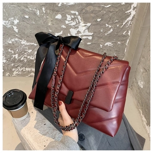 Détails de la texture matelassée bordeaux avec gros nœud noir et bandoulière chaîne