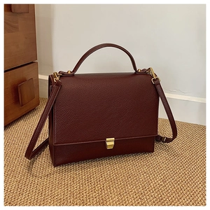 Detail view of burgundy pebble leather texture and gold metal clasp on square handbag