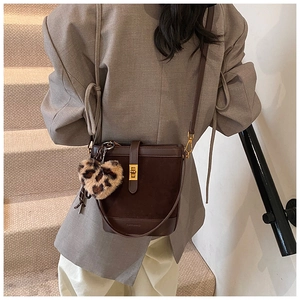 Detail of dark brown bucket bag with leopard heart charm worn by model in grey suit