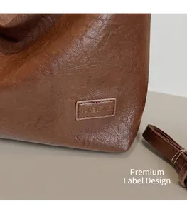 Dettaglio della borsa in pelle marrone con texture litchi e toppa con logo goffrato