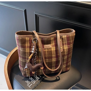 Detail of checkered wool tote bag with leather straps and dachshund charm on chair