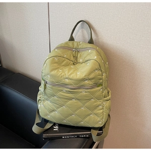 Détail d'un sac à dos en nylon matelassé vert avec broderie nœud sur un banc