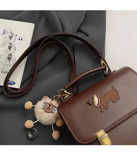 Detail of dark brown leather satchel featuring a dog embroidery and gold metal clasp