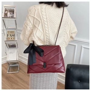 Détail d'un sac matelassé bordeaux avec un nœud en satin noir et une bandoulière chaîne