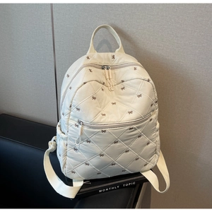 Détail du sac à dos matelassé beige avec broderies de nœuds bruns et poche avant