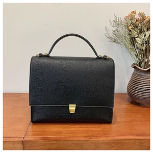 Close-up of black pebble leather texture and gold metal lock on a vintage square bag