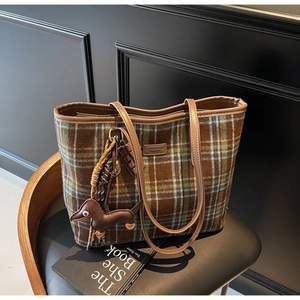 Close-up of a plaid tote bag with cute dog charms on a stylish black leather chair