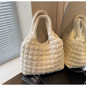 Close-up of cream quilted tote bag with puffer cube texture on a book background