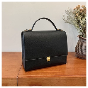 Detail of black pebbled leather texture and gold metal clasp on a vintage handbag
