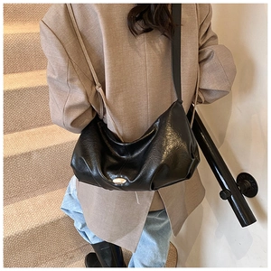 Détail du sac hobo plissé en cuir PU noir brillant porté par un mannequin en blazer beige