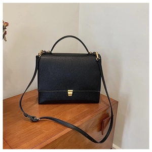 Close-up of black lychee grain leather texture and elegant gold metal buckle on handbag