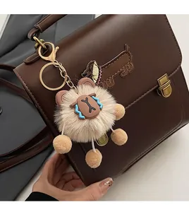 Detail view of a fluffy plush bear charm with gold hardware hanging on a brown bag