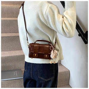 Detail der braunen Boston-Tasche mit goldenen Schnallen und einem Plüschanhänger