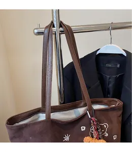 Detail of brown faux suede tote bag with embroidery, long shoulder straps and plush charm