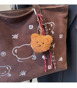 Detailed plush bear charm with woven ropes on a brown suede tote bag accessory